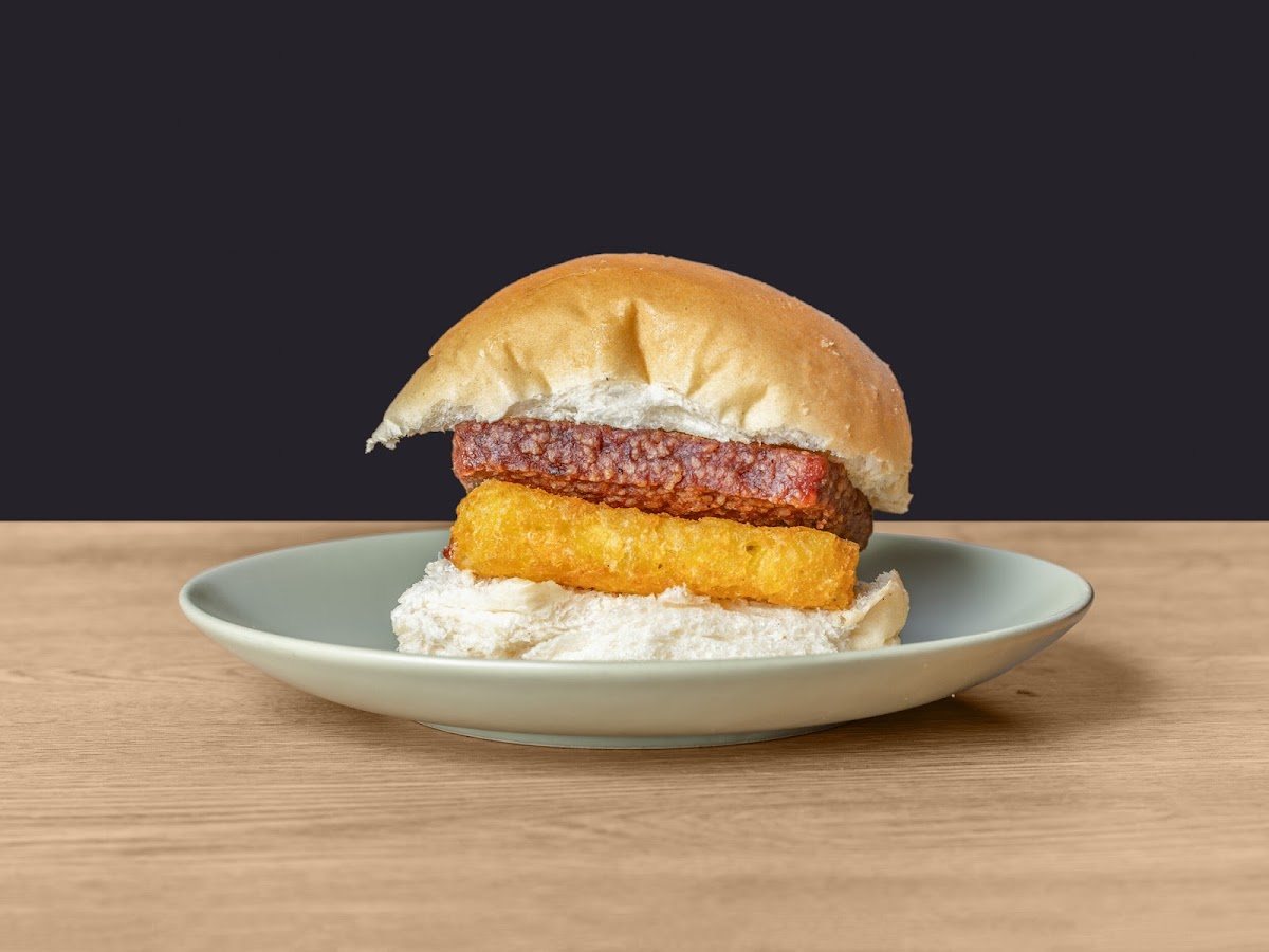 A soft floury roll filled with a slice of square sausage and a golden hash brown, on a sage-green plate.