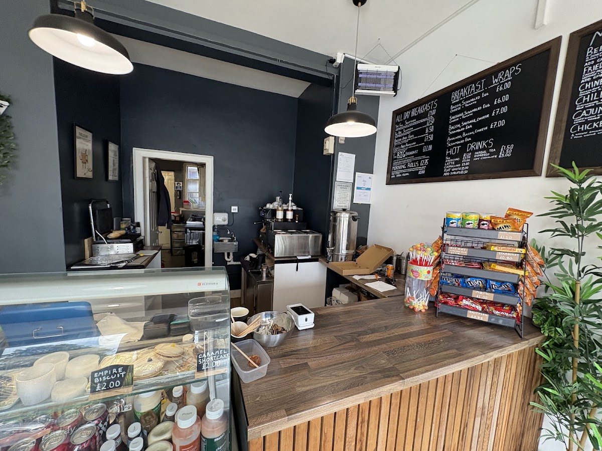 The counter from the other side: chalkboard menus on the wall, pendant lamps, a snack rack, a pot plant and the cake cabinet.